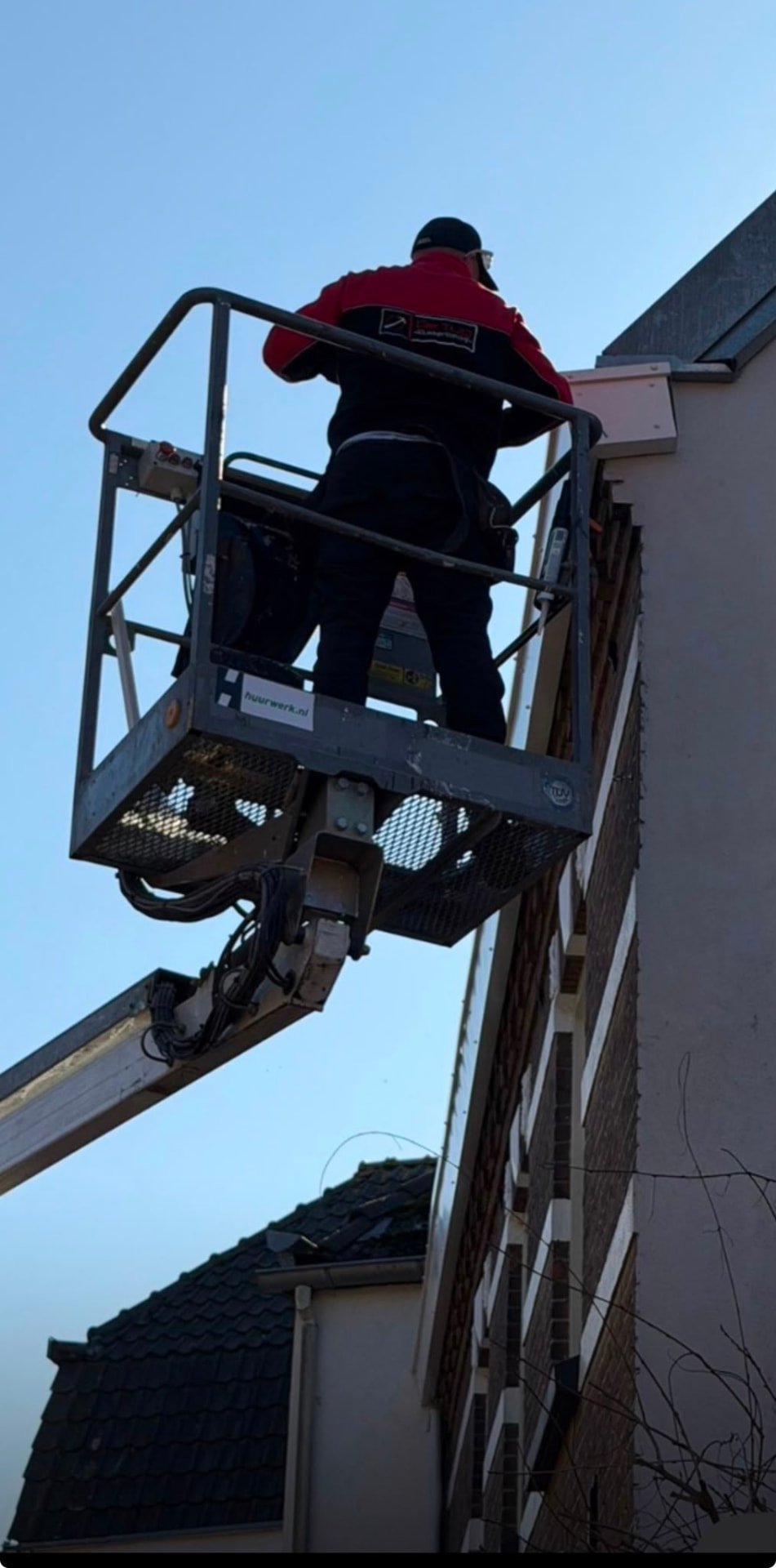 Vakman van De Tulp werkt vanuit een hoogwerker aan een dakrand